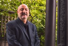 Anthony DeCurtis in black suit and shirt smiling at camera outside of building