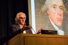 Stephen Fried lectures from a podium in from of a projection of a painting Benjamin Rush with white cursive handwriting overlaid.