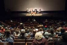 Audience looks on four speakers, seated, onstage during the No Mud, No Lotus film series