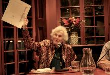 Naomi Replansky at the Kelly Writers House, speaking into microphone while holding a paper in the air for audience to see