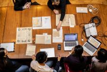 Session of Manuscript Collective session, where students and Peter Stallybrass examine documents on a wooden table in the Lea Library