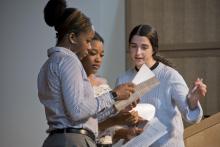 Three students stand together, speaking while consulting printed papers