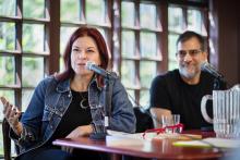 Rosanne Cash speaks into microphone while sitting at a table at the Kelly Writers House next to Al Filreis