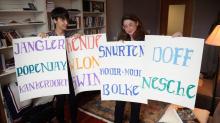 From video: Emily Steiner and Aylin Malcolm in academic office in front of bookcases hold up four white posters with 11 hand-lettered words written in  bright-colored marker