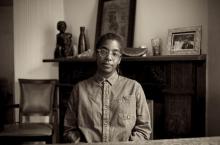 Sepia tone photography of Simone White sitting in chair with fireplace and art in background