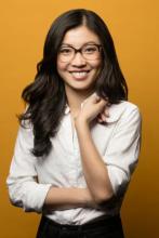 Weike Wang in white shirt, smiling at camera, in front of a yellow wall