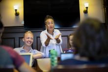 Lorene Cary (standing) responds to a student in the nine-person class, while senior James Meadows smiles off camera while seated to her right.