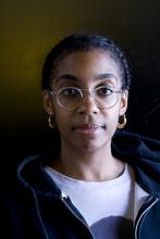 Headshot of Simone White wearing a white shirt, black hoodie, glasses, and gold earrings.