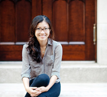 Weike Wang sitting on stairs, legs crossed, smiling, in front of wooden doors