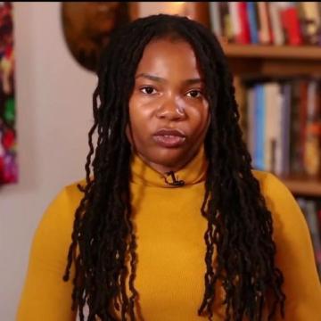 From video: Davis in yellow sweater in front of bookshelves and a painting, with "PBS NEWSHOUR," "#PBSNEWS," and the logo in the bottom left corner 