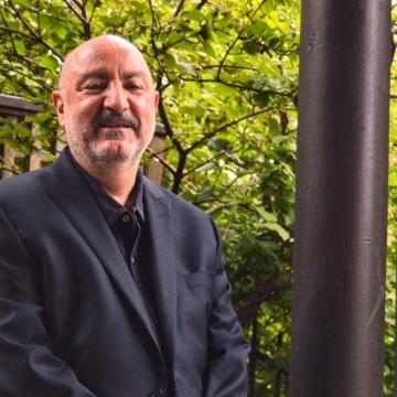 Anthony DeCurtis in black suit and shirt smiling at camera outside of building