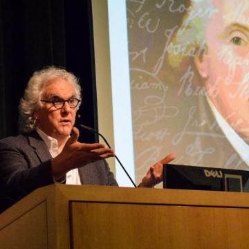 Stephen Fried lectures from a podium in from of a projection of a painting Benjamin Rush with white cursive handwriting overlaid.