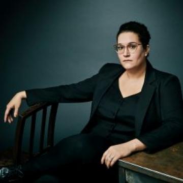 Carmen Maria Machado in black suit sitting in front of blue wall