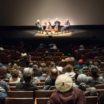 Audience looks on four speakers, seated, onstage during the No Mud, No Lotus film series