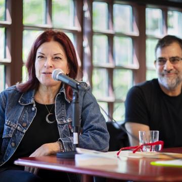 Rosanne Cash speaks into microphone while sitting at a table at the Kelly Writers House next to Al Filreis