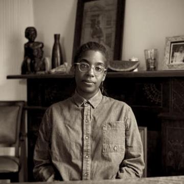 Sepia tone photography of Simone White sitting in chair with fireplace and art in background