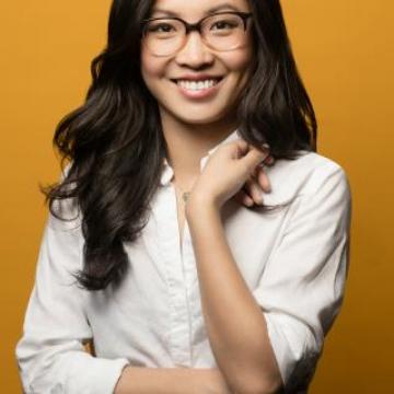 Weike Wang in white shirt, smiling at camera, in front of a yellow wall