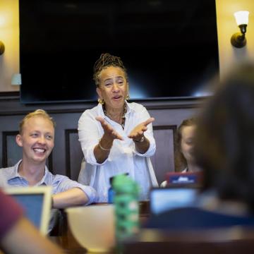 Lorene Cary (standing) responds to a student in the nine-person class, while senior James Meadows smiles off camera while seated to her right.